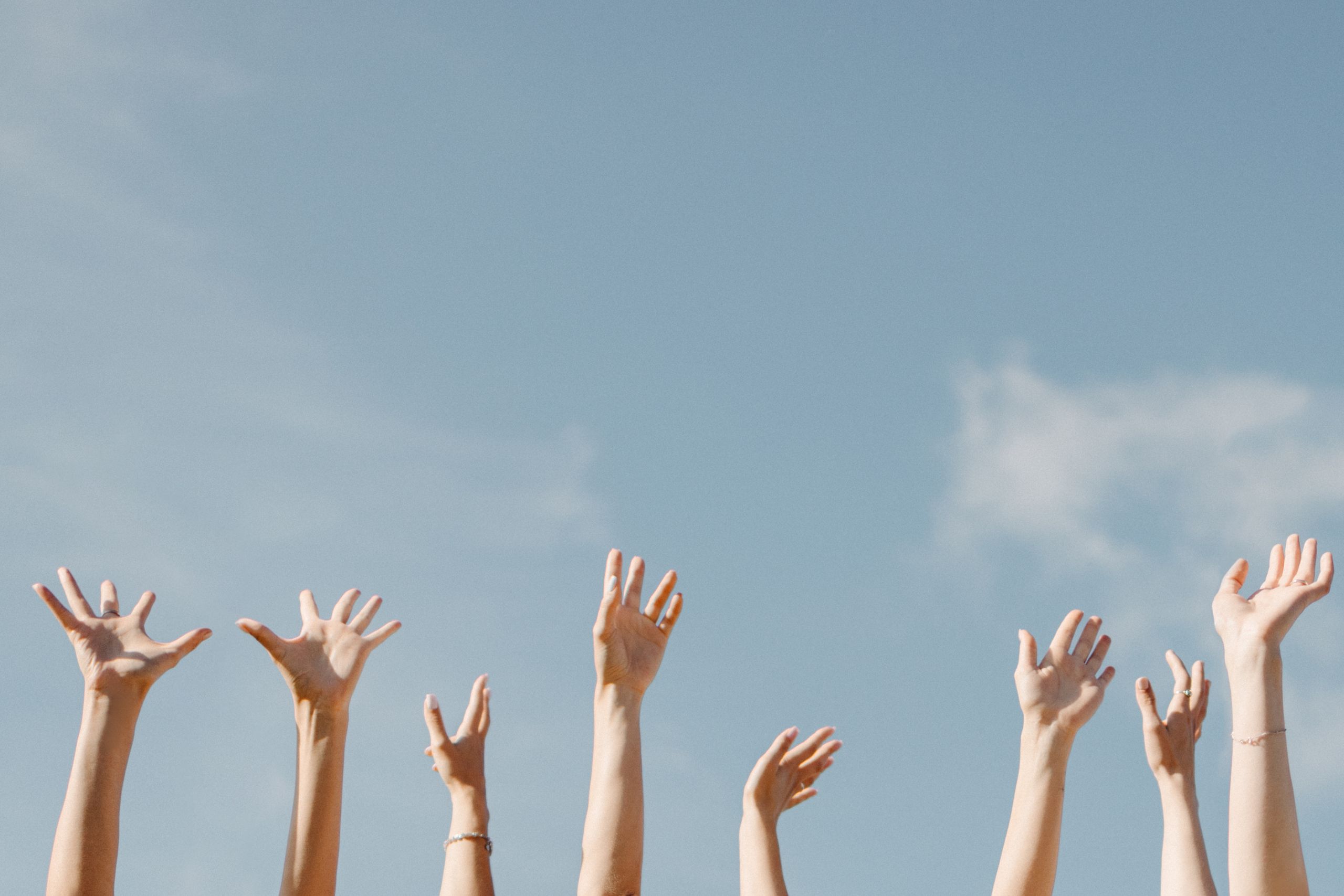 Multiple hands reaching toward the sky, symbolizing freedom and unity in a clear blue backdrop.